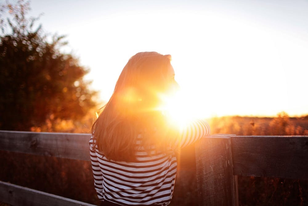 Woman standing outside next to fence looking at sunrise