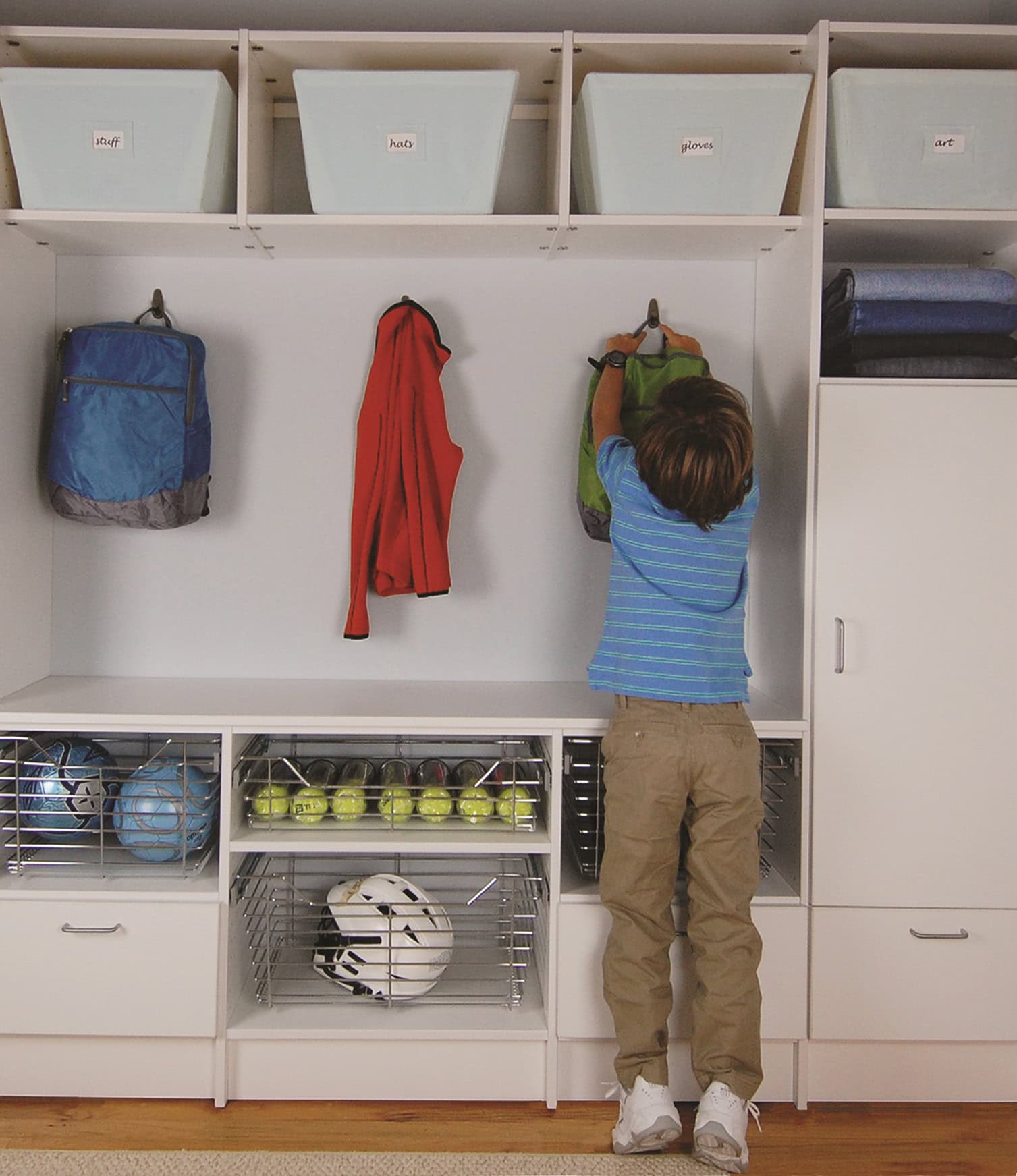 child reaching up in a mudroom to grab his backpack